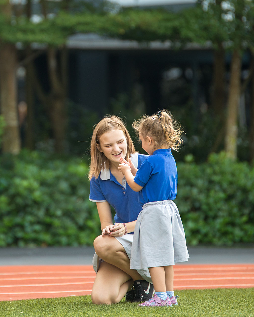 A female OFS High School student kneeling in front of a female OFS Kindergarten student on the field