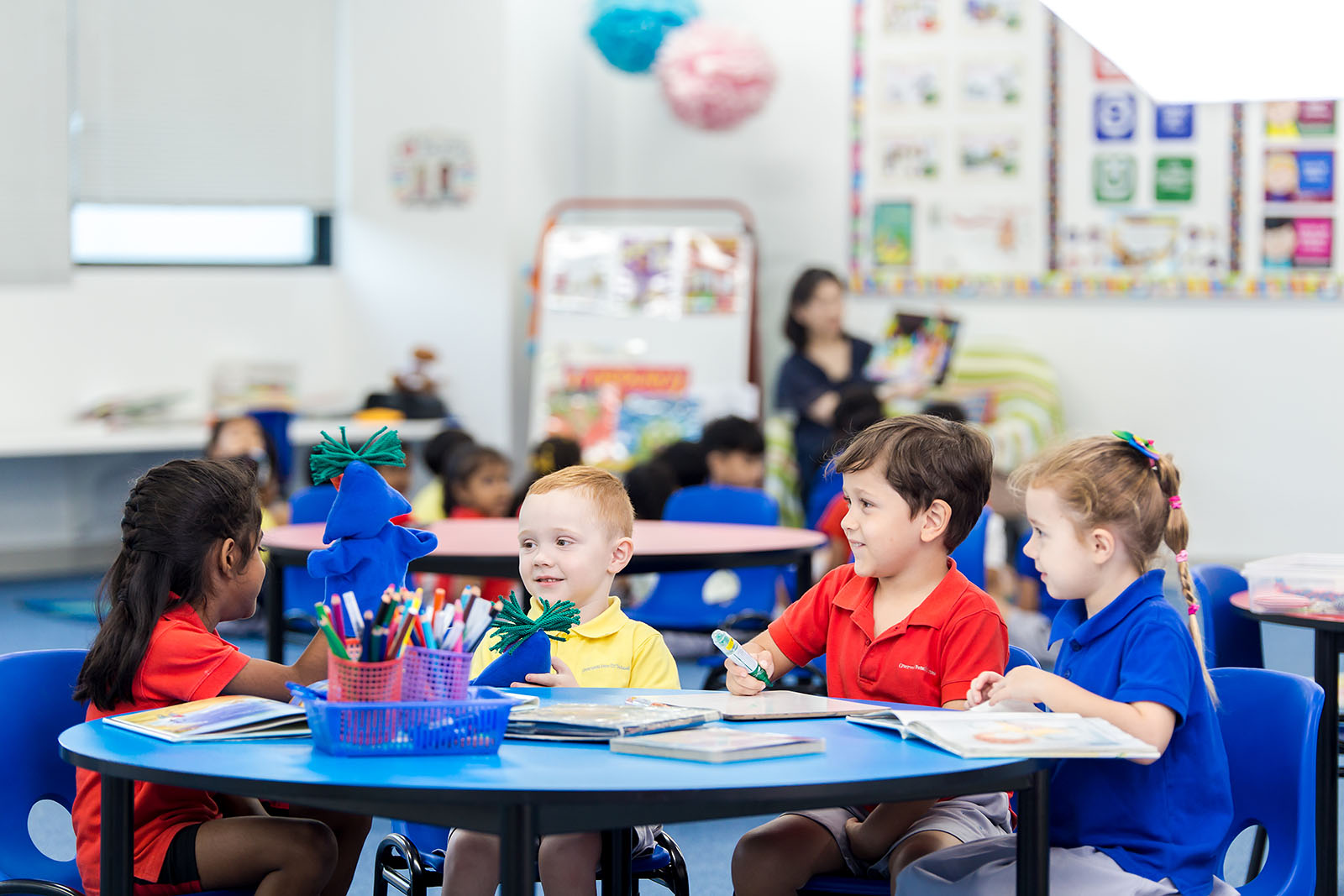 Four OFS Kindergarten students sitting around a round table and smiling while studying in the Kindergarten library