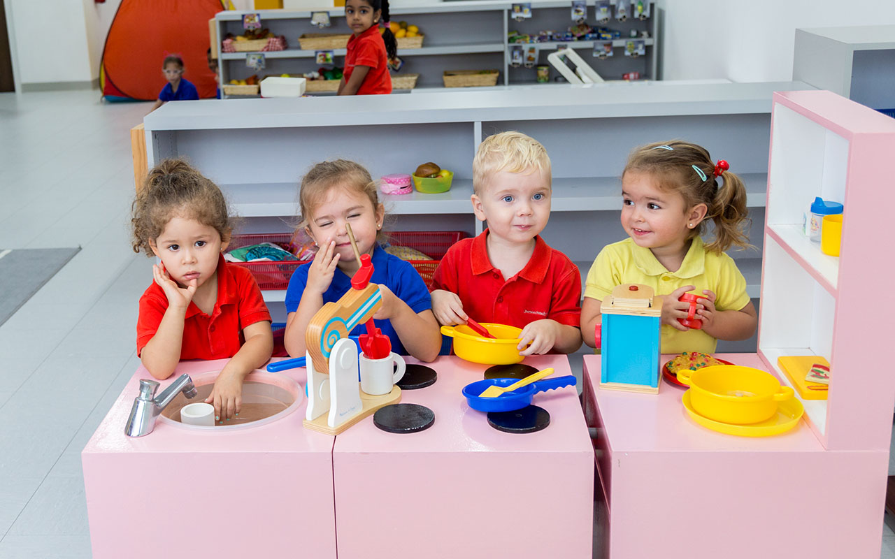 Four OFS Kindergarten students playing cooking with the toy kitchen set