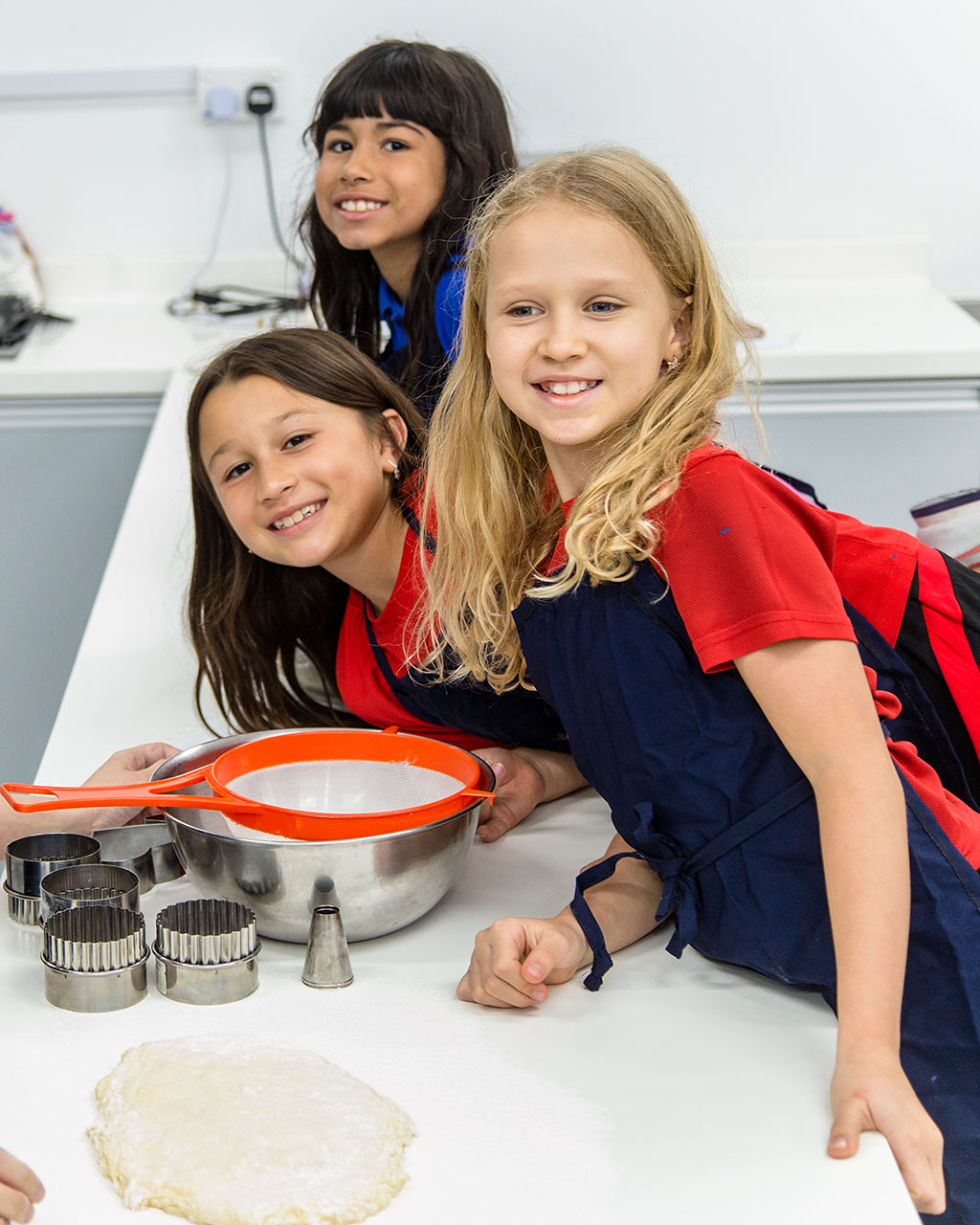 Three female OFS Elementary School students smile to the camera during baking enrichment class