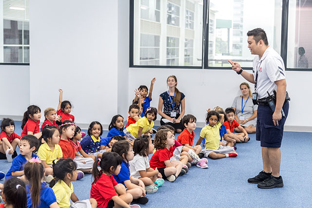OFS Kindergarten students listening to a policeman in the activity room