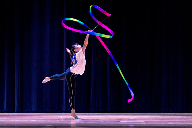 OFS High School student performing gymnastics ribbon routine on the auditorium stage